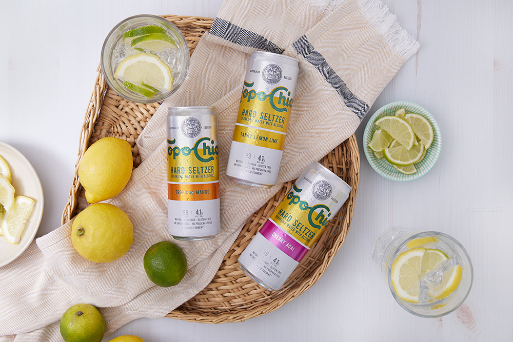 Topo Chico Hard Seltzer Dosen in 3 Sorten mit Zitronen und Limetten daneben